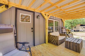 A covered porch with a wooden bench, a table, and a door. - Lake Tawakoni Basecamp: Covered Patio + Fire Pit! (Wills Point)