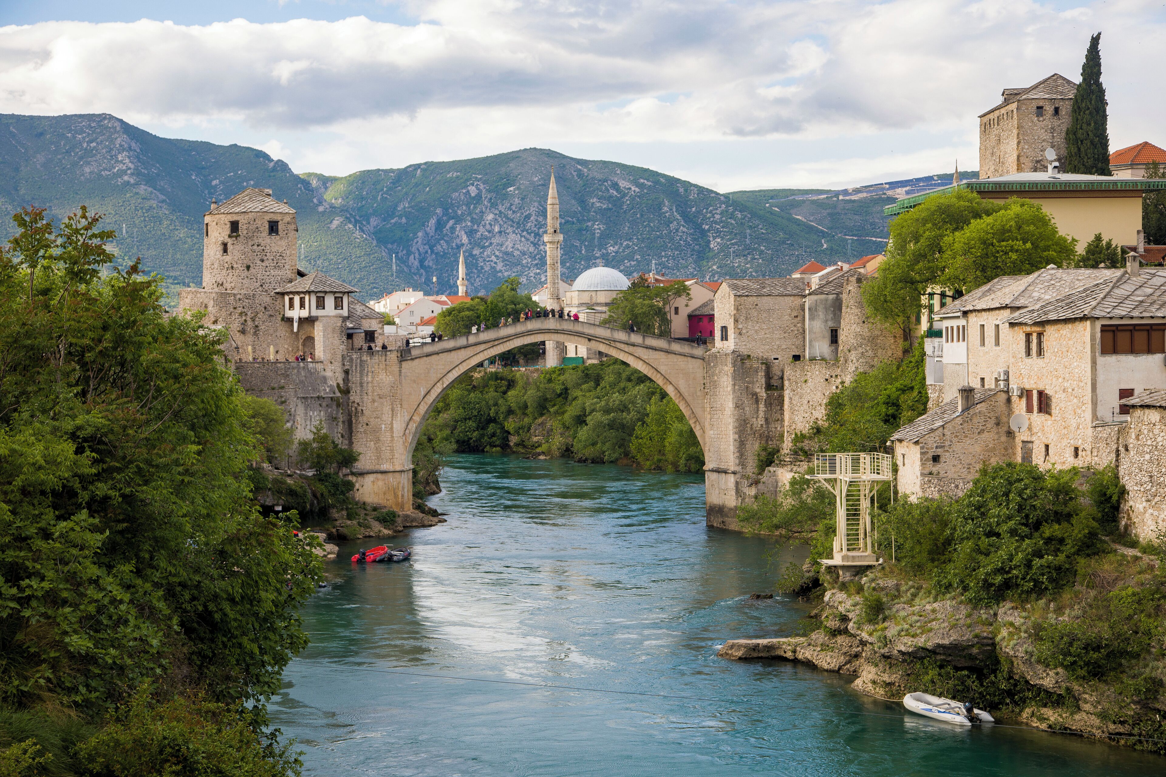 Un pont de pierre enjambant une rivière, des bâtiments historiques et une mosquée dotée d’un minaret.