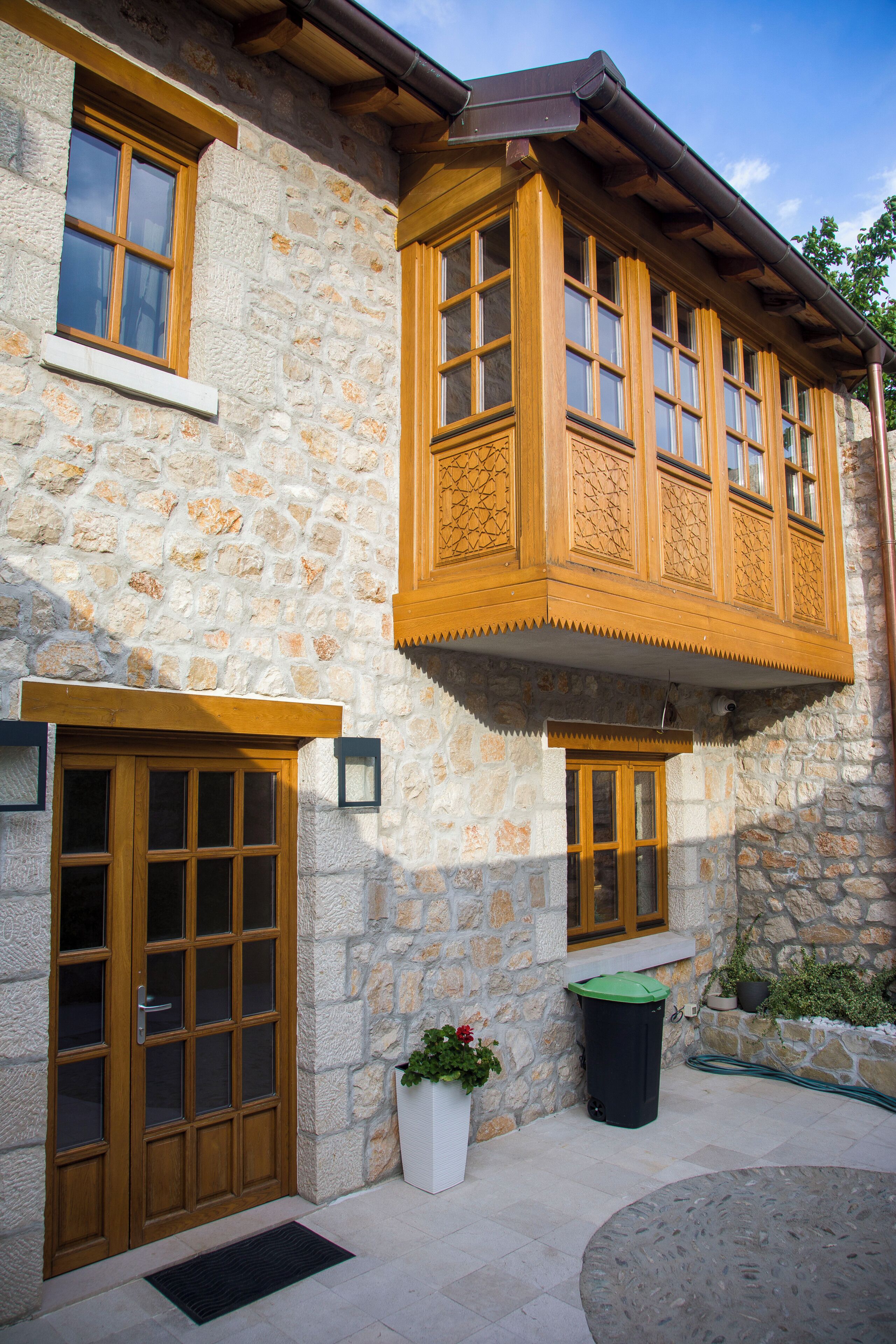 A stone building with wooden windows and doors, a small outdoor seating area, and a potted plant.