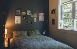 A bedroom with a bed, a bedside lamp, a window, and various wall art. - Artist’s EcoRetreat in the heart of Ballard (Seattle)