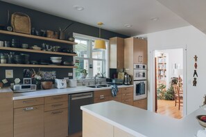 A modern kitchen with wooden cabinets, a dishwasher, and a large window. - Artist’s EcoRetreat in the heart of Ballard (Seattle)