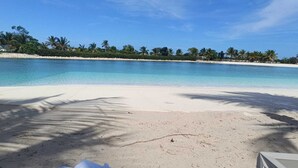 Ein Strand mit klarem türkisblauem Wasser, weißem Sand und Palmen.