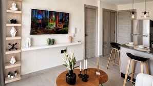 Ein modernes Wohnzimmer mit Flachbildfernseher, Couch, Couchtisch mit Kerzen und einer Küchenzeile mit Barhocker.