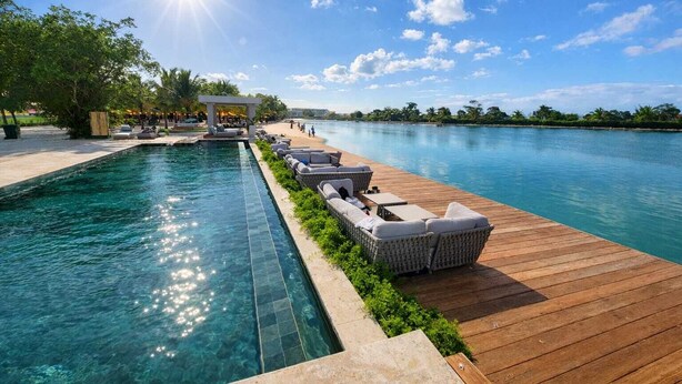 Ein Schwimmbecken mit Holzterrasse und Liegestühlen, umgeben von viel Grün und Palmen.
