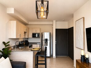A modern kitchen with a central island, stainless steel appliances, and a hanging light fixture. - Modern Apartment on a High Floor in Santa Tecla (Santa Tecla)