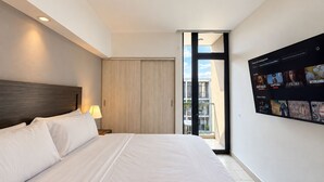 A hotel room with a large bed, a nightstand with a lamp, a sliding door to a balcony, and a wall-mounted TV displaying various channels. - Santa Tecla | Modern high-floor apartment (Santa Tecla)