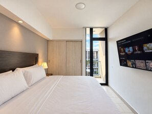 A hotel room with a large bed, a nightstand with a lamp, a sliding door to a balcony, and a wall-mounted TV displaying various channels. - Santa Tecla | Modern high-floor apartment (Santa Tecla)