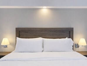 A neatly made bed with a wooden headboard, two bedside lamps, and a wall-mounted light above the bed. - Santa Tecla | Modern high-floor apartment (Santa Tecla)