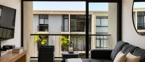 Un salon moderne avec un canapé, un téléviseur et un balcon agrémenté de plantes.