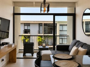 A modern living room with a sofa, a TV, and a balcony with plants. - Santa Tecla | Modern high-floor apartment (Santa Tecla)