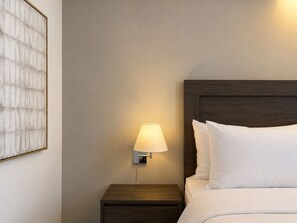 Ein Hotelzimmer mit Holz-Kopfteil, einer Nachttischlampe und einem gerahmten Kunstwerk an der Wand.