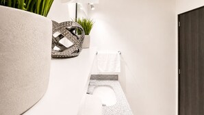 A modern bathroom with a toilet, a towel rack, a potted plant, and a decorative metal piece. - Santa Tecla | Modern high-floor apartment (Santa Tecla)