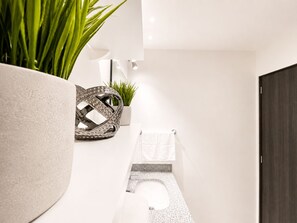 A modern bathroom with a toilet, a towel rack, a potted plant, and a decorative metal piece. - Santa Tecla | Modern high-floor apartment (Santa Tecla)