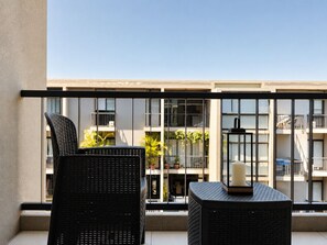Ein Balkon mit Korbmöbeln, einer Kerze und Blick auf ein Gebäude mit Balkonen und Pflanzen.