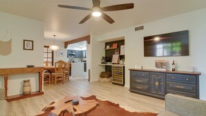 Un amplio salón con una mesa de comedor, sillas, un sofá, una mesa de centro, una chimenea, un ventilador de techo, un televisor y una cocina al fondo.