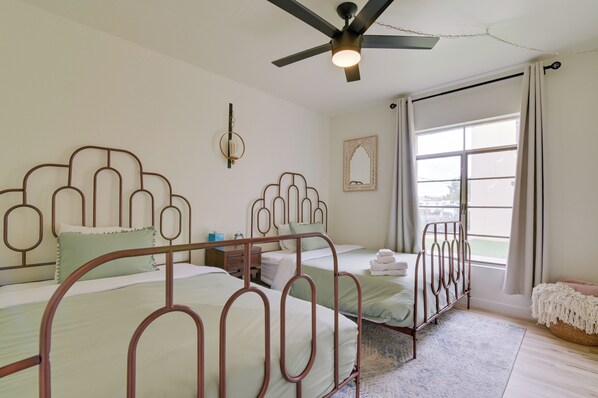 A bedroom with two metal-framed beds, a ceiling fan, a large window with curtains, and a wall-mounted mirror. - 4 Mi to Old Town! Extended Desert Escape w/ Pool (Phoenix)