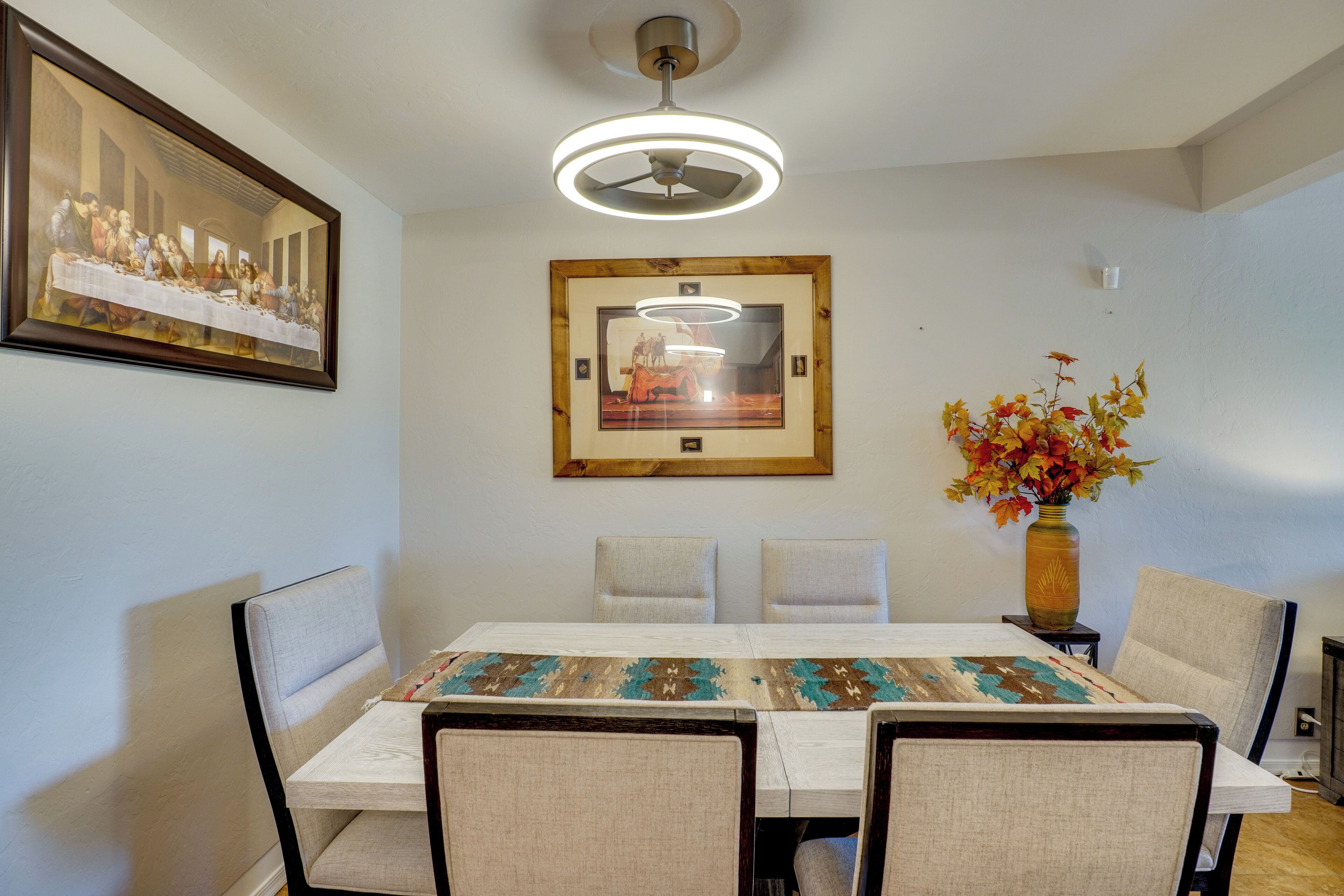 A dining area with a table, chairs, a ceiling fan, and framed artwork on the walls.