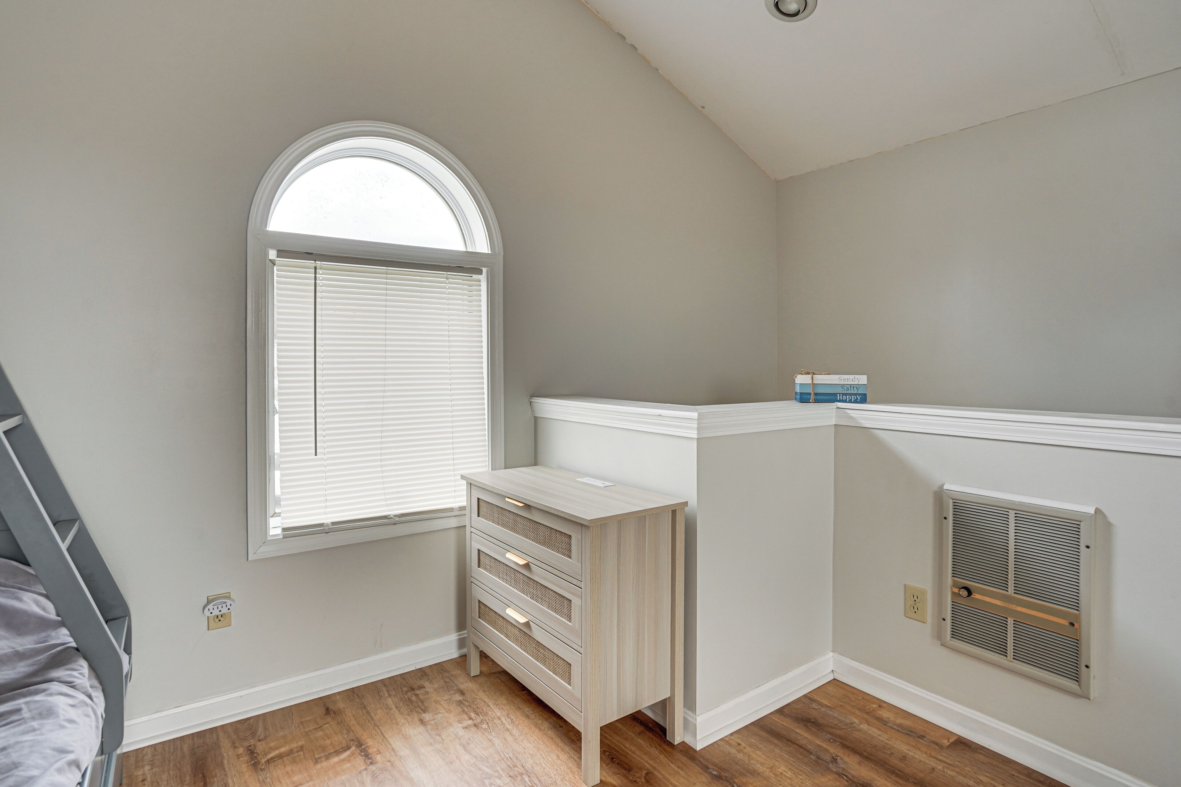 Een kamer met een raam, een dressoir, een radiator en een houten vloer.