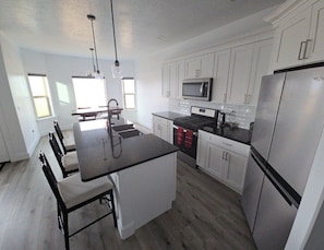 A modern kitchen with white cabinets, stainless steel appliances, a black countertop island, and a dining area with chairs.