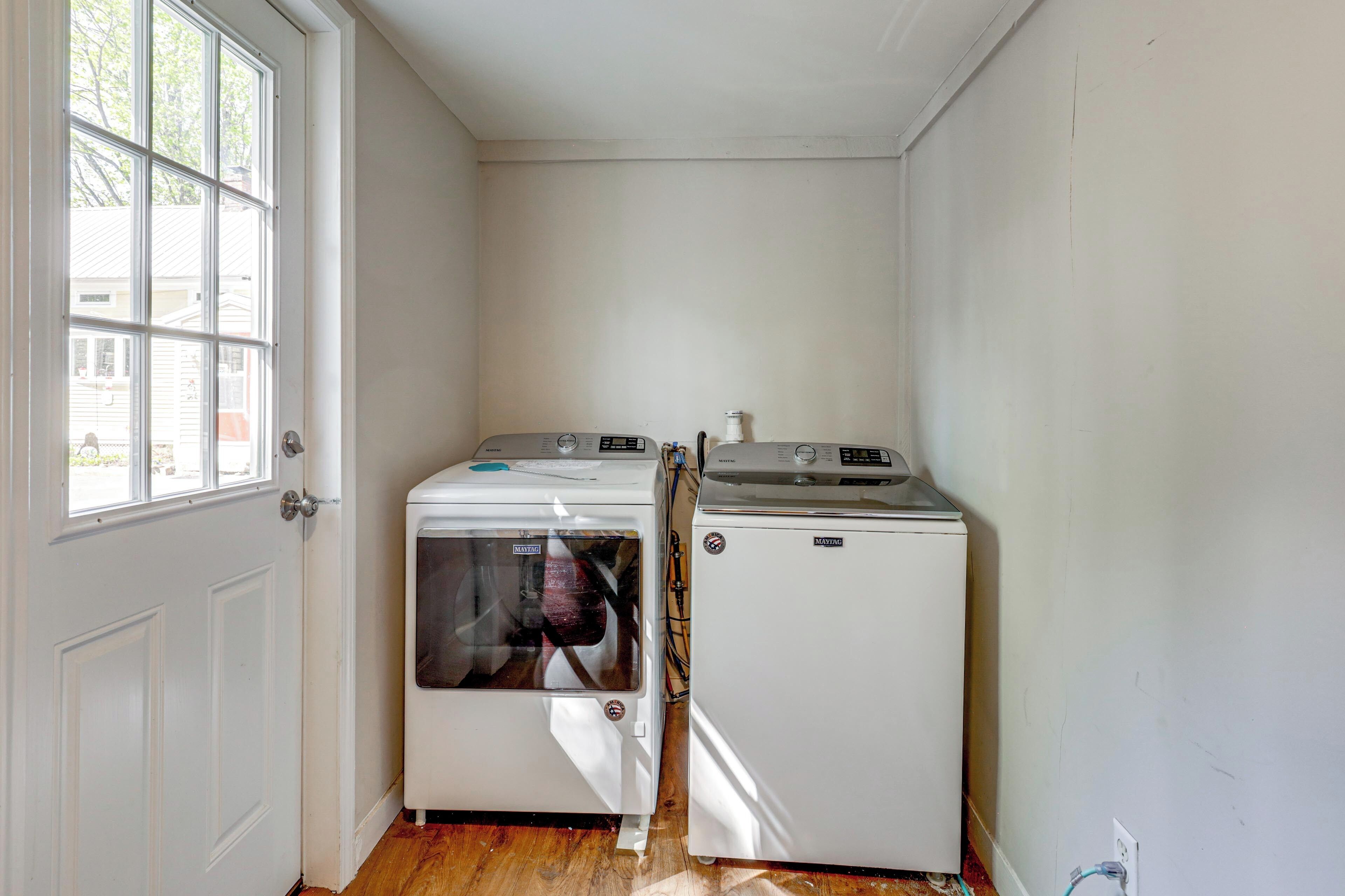 A laundry room with two white appliances, a door with a window, and a wall with a visible electrical outlet.