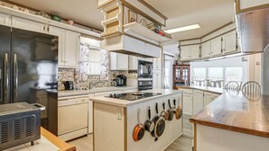 Una cucina con mobili bianchi, un frigorifero in acciaio inossidabile, forno integrato e un'isola centrale con pentole appese.