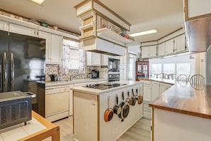 Eine Küche mit weißen Schränken, einem Edelstahl-Kühlschrank, einem eingebauten Backofen und einer Kochinsel mit hängenden Töpfen.