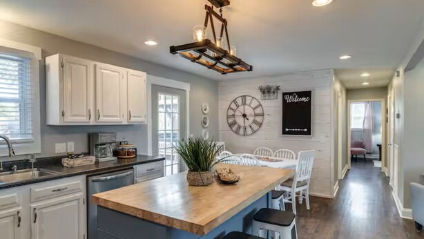 Una cocina con armarios blancos, una isla de madera y un reloj en la pared.