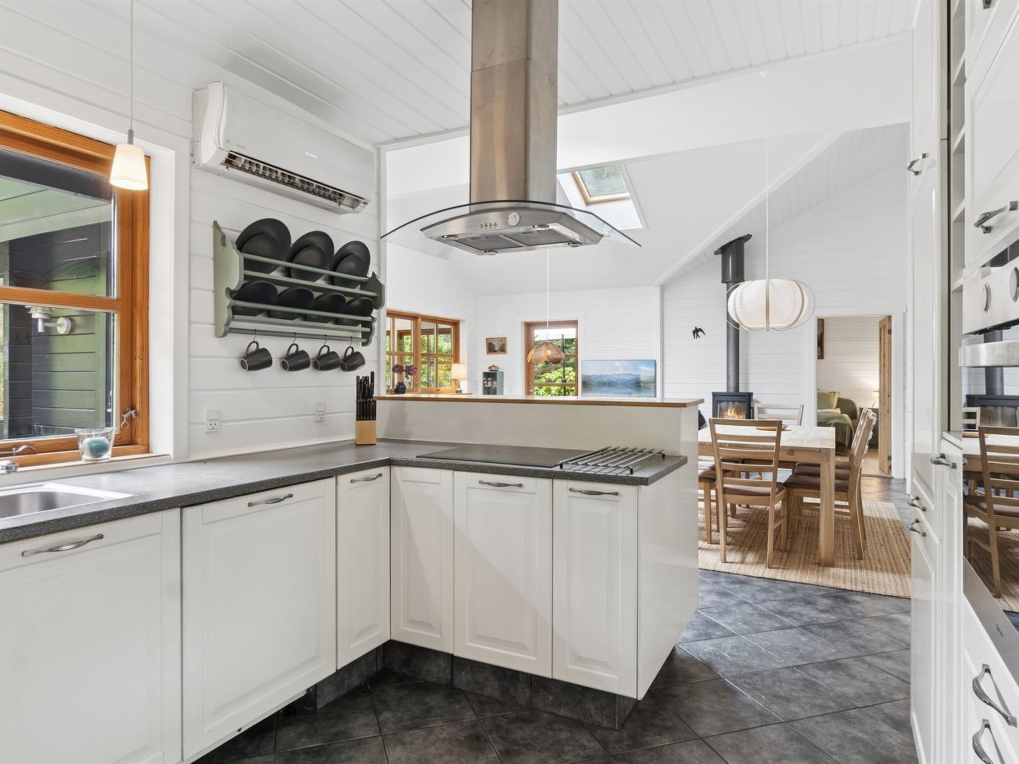 Une cuisine moderne avec des meubles blancs, un îlot central, une cuisinière encastrée et une grande fenêtre.