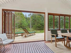 A wooden deck with outdoor furniture, large windows, and a view of a forest. - "Pertti" - 625m from the sea by Interhome (Højby)