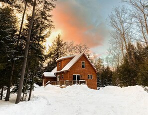 A wooden cabin surrounded by snow-covered ground and trees. - 12 min Sunday River! HotTub, Pet Friendly, Firepit (Bethel)
