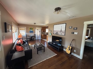 Ein Wohnzimmer mit Sofa, Couchtisch, Fernseher und Gitarre.