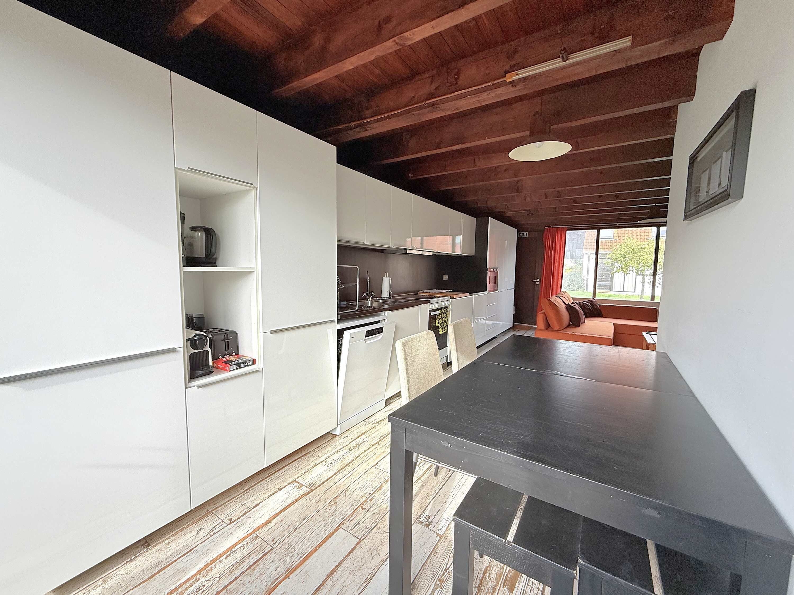 A modern kitchen with white cabinetry, a wooden floor, and a black countertop.