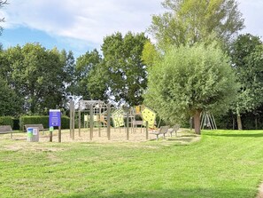 Une aire de jeux avec des structures d’escalade et des balançoires, entourée d’arbres et d’une pelouse.