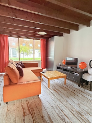 Una sala de estar con sofá, mesa de centro de madera, televisor y refrigerador.