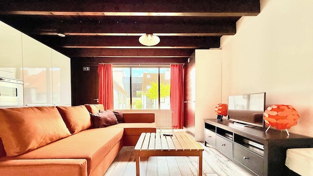 A modern living room with a sofa, wooden coffee table, TV stand, and a window with curtains.