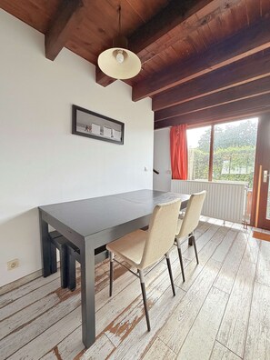 Un área de comedor con una mesa y sillas, una lámpara de techo, un cuadro en la pared y una ventana con cortinas.