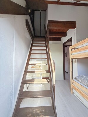 Un escalier en bois mène à une chambre mansardée équipée d’un lit superposé.
