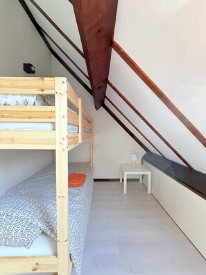 A small, single-bedded room with a sloped ceiling, a white desk, and a patterned bedspread.