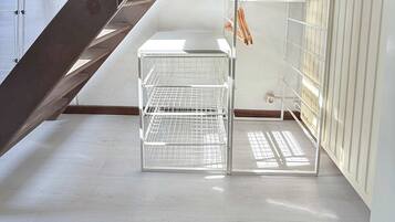 Une pièce avec un plafond en pente, un radiateur blanc et une étagère en métal.