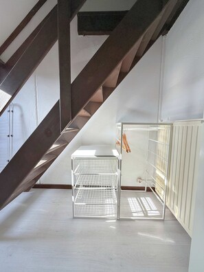 Una habitación con techo inclinado, un radiador blanco y una estantería metálica.