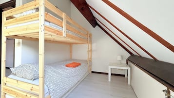 Un lit superposé dans une pièce avec un plafond en pente, une petite table de chevet avec une lampe et un mur blanc.