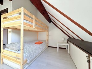 Un lit superposé dans une pièce avec un plafond en pente, une petite table de chevet avec une lampe et un mur blanc.