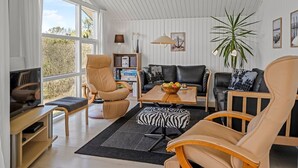 Ein modernes Wohnzimmer mit großem Fenster, einer Ledersofa, einem Holztisch und einem Bücherregal.