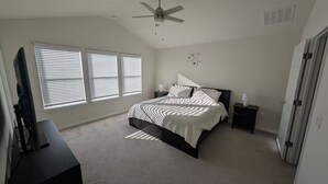 Une chambre à coucher avec un lit, un ventilateur de plafond, un bureau avec un ordinateur et une télévision.