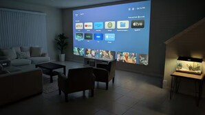 Un salon avec un grand écran affichant l’interface d’une application multimédia, un canapé, une table basse et une petite table avec une lampe.