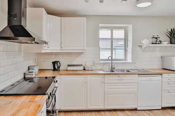 A modern kitchen with white cabinetry, a black stove, a dishwasher, and a window with blinds. - Limehouse Eco Guesthouse (Slane)