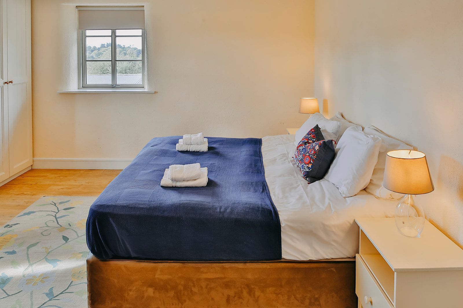 A hotel room with a bed, bedside lamps, a window, and a door.