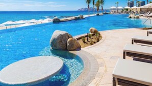 A resort pool with a view of the ocean, lounge chairs, and palm trees. - Luxury Cabo Escapes Suites, Villas & Elevated Experiences by Chez Tandrie (San José del Cabo)