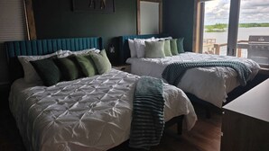 Une chambre d’hôtel avec deux lits, une œuvre d’art représentant un élan, une vue sur l’eau et une terrasse en bois à l’extérieur.