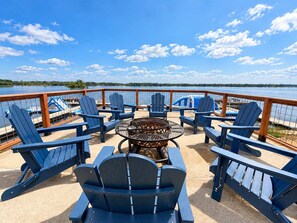 A deck with Adirondack chairs and a fire pit, overlooking a body of water.